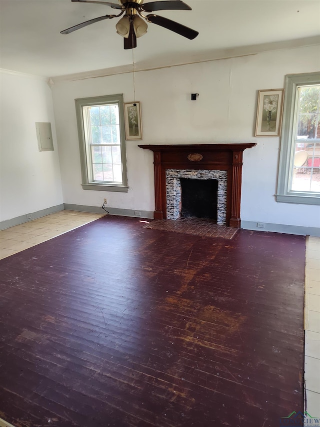 unfurnished living room featuring a tile fireplace, electric panel, ceiling fan, and a healthy amount of sunlight