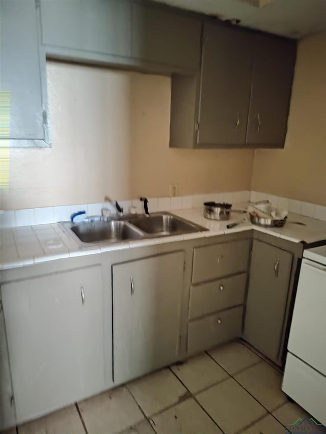 kitchen with sink, light tile patterned floors, range, gray cabinets, and tile counters