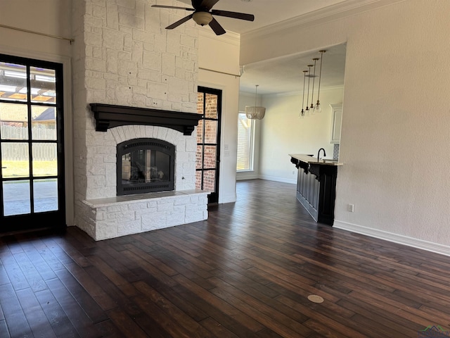 unfurnished living room featuring ceiling fan, a fireplace, ornamental molding, and dark wood-type flooring