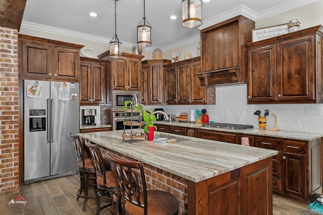 kitchen featuring stainless steel appliances, light stone counters, backsplash, an island with sink, and decorative light fixtures