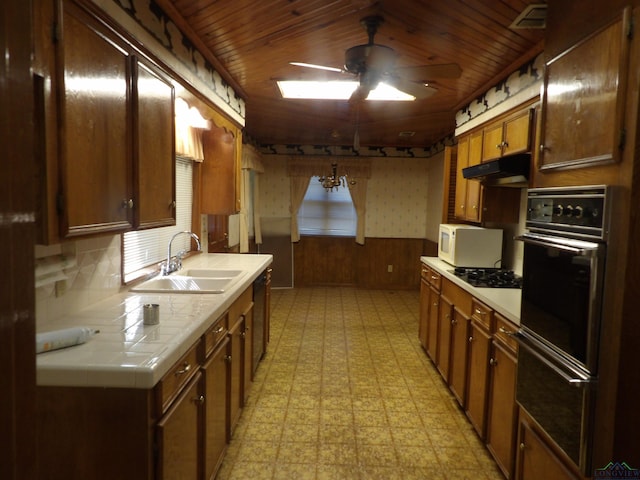 kitchen featuring a skylight, wooden walls, sink, black appliances, and tile countertops