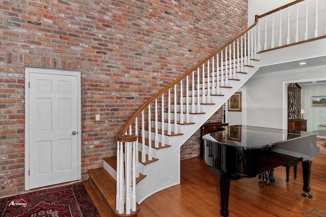 stairs with wood-type flooring, a towering ceiling, crown molding, and brick wall