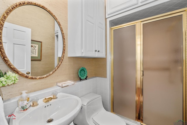 bathroom featuring toilet, a shower with shower door, and sink