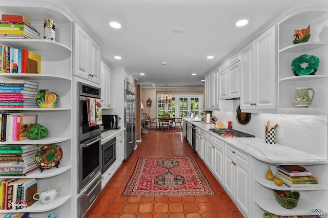 kitchen with decorative backsplash, light stone countertops, built in appliances, white cabinets, and hanging light fixtures