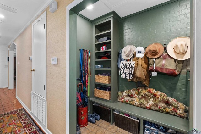 mudroom with built in shelves, brick wall, and ornamental molding