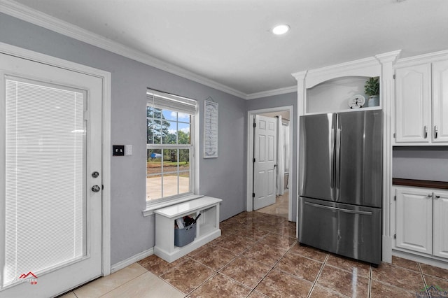 kitchen featuring stainless steel refrigerator, white cabinetry, crown molding, and dark tile patterned flooring