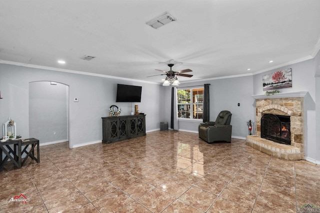 tiled living room featuring a stone fireplace, ceiling fan, and crown molding