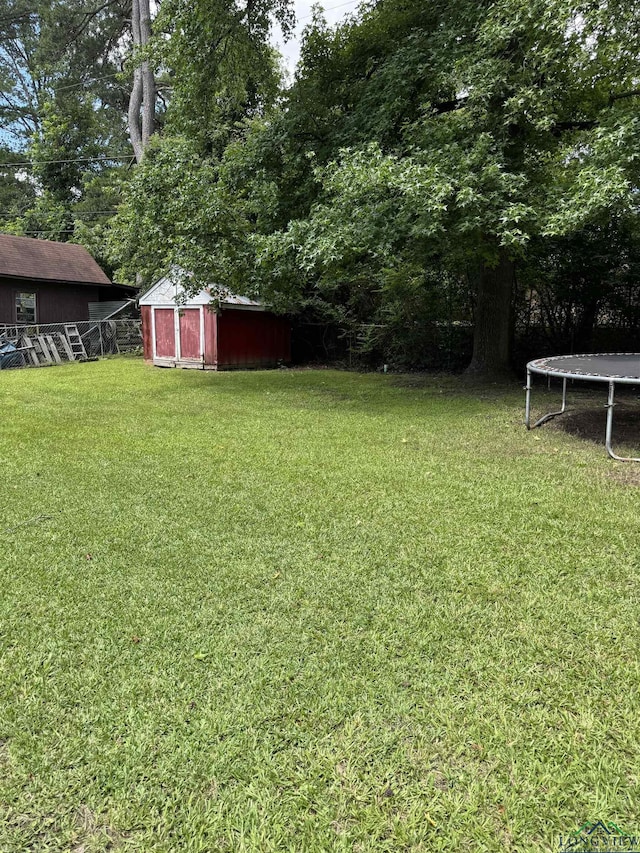 909 Stewart St, Atlanta, TX 75551 - view of green lawn with a trampoline, a storage unit, and view of wooded area