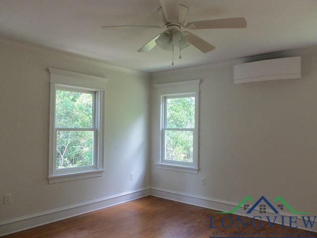 unfurnished room with a wall unit AC, plenty of natural light, dark hardwood / wood-style floors, and ornamental molding