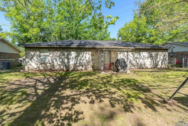 back of house featuring brick siding, a lawn, and fence
