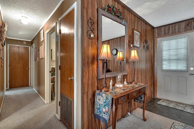 corridor with crown molding, a textured ceiling, wood walls, and visible vents