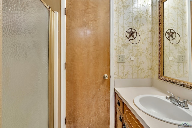 bathroom with wallpapered walls, vanity, and an enclosed shower