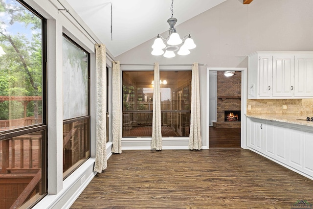 unfurnished dining area with a chandelier, dark hardwood / wood-style flooring, a fireplace, and vaulted ceiling