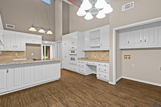 kitchen with light stone counters, double oven, decorative light fixtures, decorative backsplash, and white cabinets