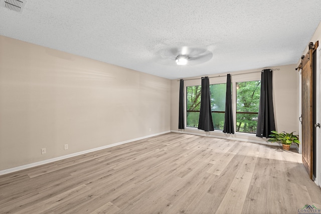 spare room featuring light wood-type flooring, a textured ceiling, and a barn door