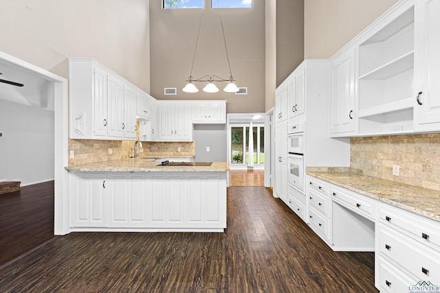 kitchen with white cabinetry, a towering ceiling, hanging light fixtures, and light stone counters