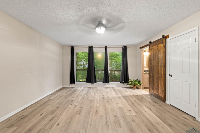 interior space with a barn door, ceiling fan, a textured ceiling, and light wood-type flooring