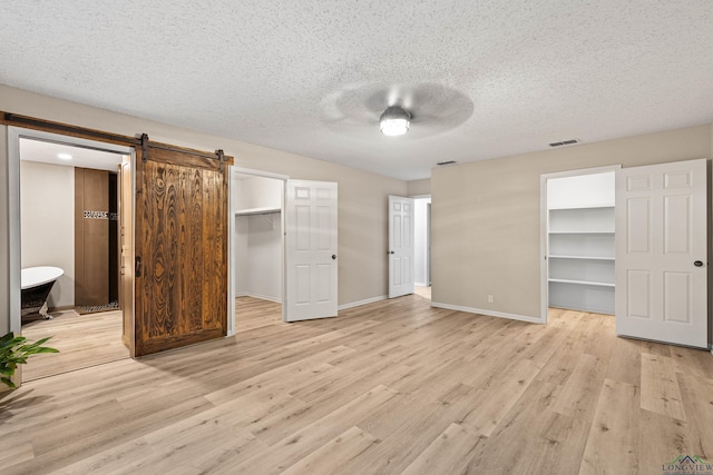 unfurnished bedroom with light wood-type flooring, ensuite bathroom, ceiling fan, a barn door, and a spacious closet