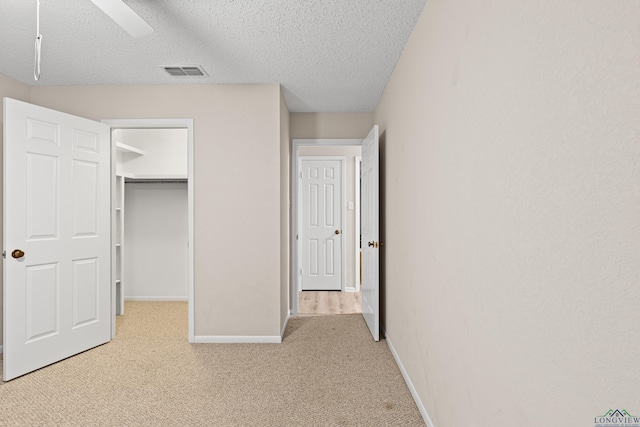 unfurnished bedroom featuring a closet, a textured ceiling, light colored carpet, and ceiling fan