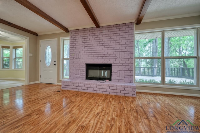 unfurnished living room featuring light hardwood / wood-style flooring, a fireplace, ornamental molding, a textured ceiling, and beamed ceiling