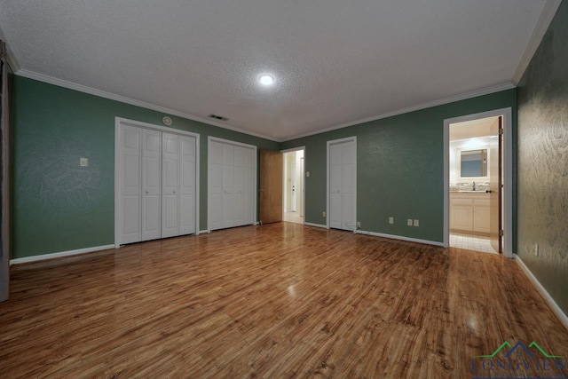 unfurnished bedroom featuring sink, wood-type flooring, a textured ceiling, multiple closets, and ornamental molding