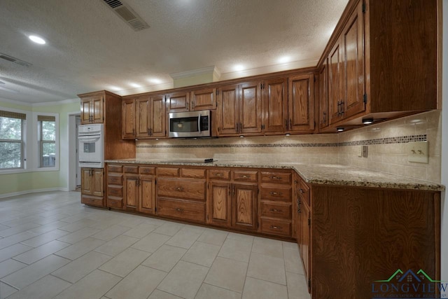 kitchen with crown molding, backsplash, oven, and light stone counters