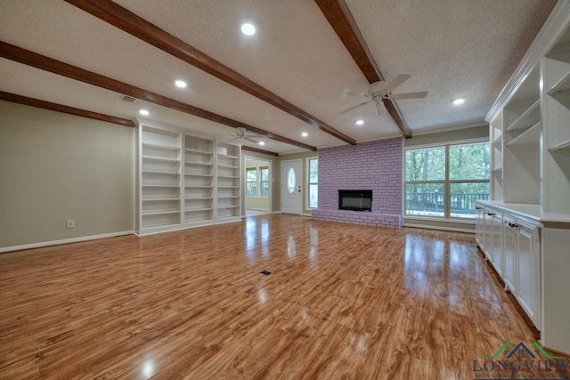 unfurnished living room featuring ceiling fan, a textured ceiling, a brick fireplace, beamed ceiling, and light wood-type flooring