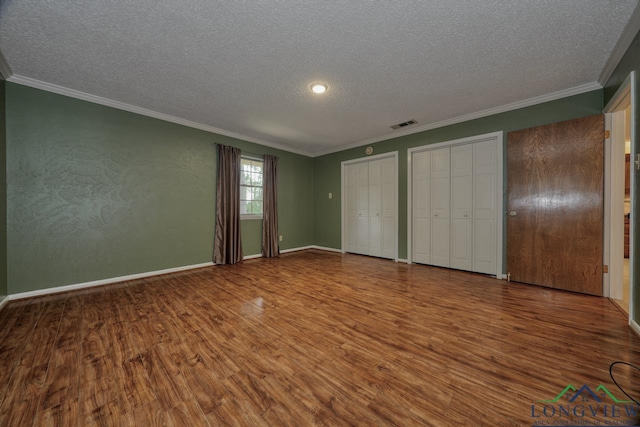 unfurnished bedroom with hardwood / wood-style floors, crown molding, a textured ceiling, and multiple closets