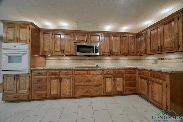 kitchen with a textured ceiling, white oven, ornamental molding, light stone countertops, and decorative backsplash