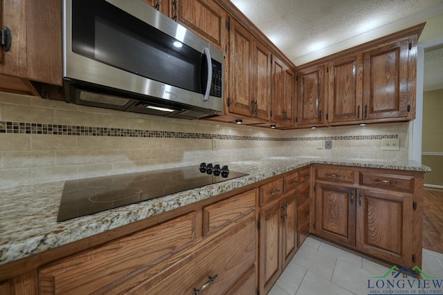 kitchen with light stone counters, tasteful backsplash, a textured ceiling, light tile patterned flooring, and black electric cooktop