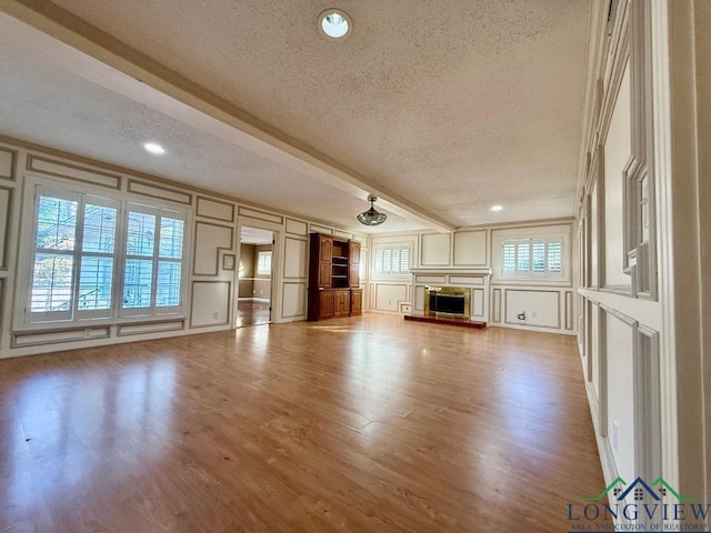 unfurnished living room featuring beamed ceiling, hardwood / wood-style floors, and a textured ceiling