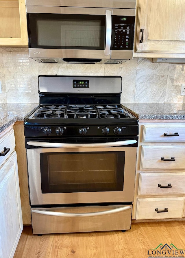 kitchen featuring light stone countertops, light brown cabinetry, backsplash, and stainless steel appliances