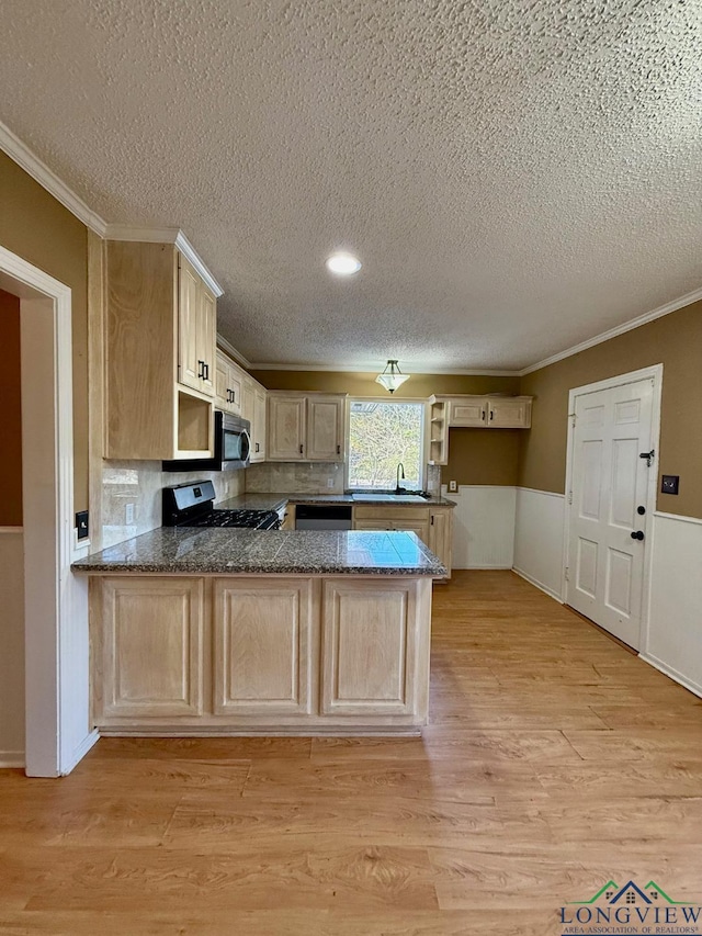 kitchen featuring kitchen peninsula, appliances with stainless steel finishes, ornamental molding, light brown cabinets, and light hardwood / wood-style floors