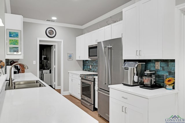 kitchen featuring backsplash, crown molding, sink, appliances with stainless steel finishes, and white cabinetry