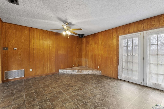 empty room featuring a textured ceiling, ceiling fan, and wood walls