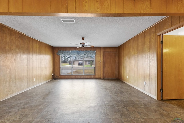 unfurnished room featuring a textured ceiling, ceiling fan, and wood walls