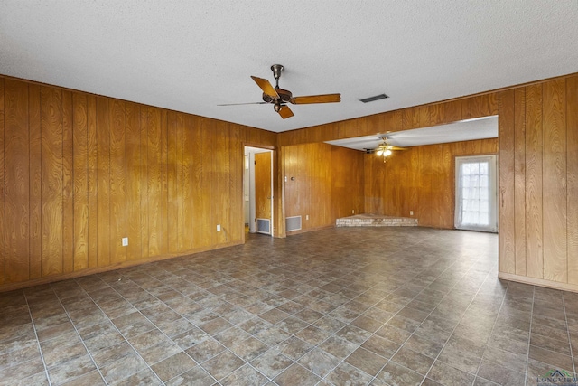 spare room featuring ceiling fan, wooden walls, and a textured ceiling