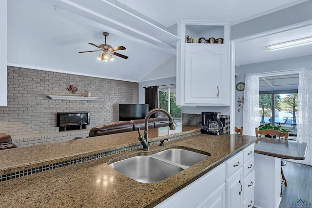 kitchen featuring sink, a brick fireplace, dark stone countertops, vaulted ceiling, and white cabinets