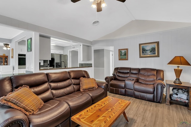 living room with ceiling fan, light wood-type flooring, and vaulted ceiling