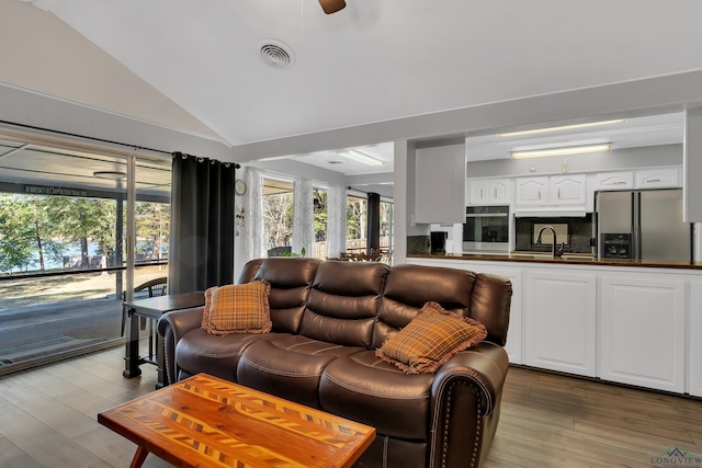 living room with ceiling fan, sink, lofted ceiling, and light hardwood / wood-style flooring