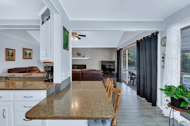 kitchen featuring ceiling fan, dark stone counters, lofted ceiling, a fireplace, and white cabinets