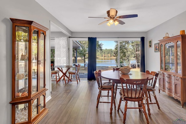 dining area featuring light wood-type flooring, a water view, and ceiling fan