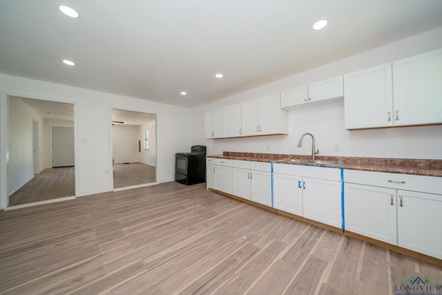 kitchen with black / electric stove, sink, light hardwood / wood-style flooring, and white cabinets