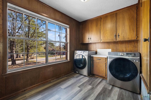 clothes washing area with wood walls, cabinets, a textured ceiling, and light hardwood / wood-style floors