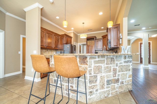 kitchen featuring kitchen peninsula, a kitchen breakfast bar, stainless steel fridge, light stone countertops, and pendant lighting