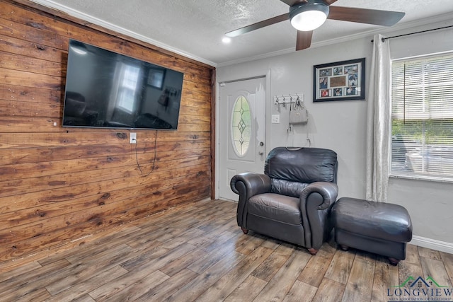sitting room featuring ceiling fan, ornamental molding, wood finished floors, and wooden walls
