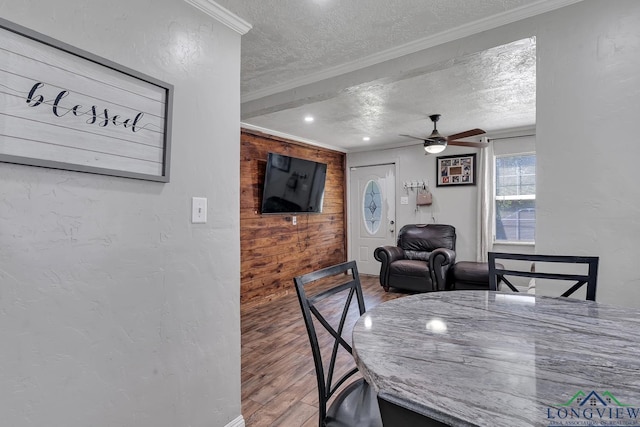 dining room with a textured ceiling, wood finished floors, ceiling fan, wooden walls, and ornamental molding