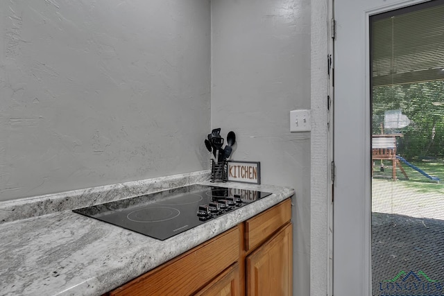 details with brown cabinetry, black electric stovetop, a textured wall, and light countertops