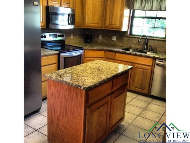 kitchen with appliances with stainless steel finishes, sink, light tile patterned floors, light stone countertops, and a kitchen island