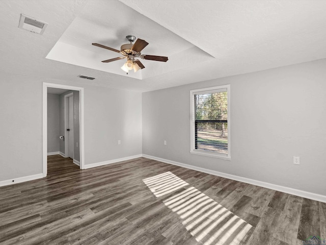 spare room featuring baseboards, visible vents, a raised ceiling, ceiling fan, and dark wood-style flooring